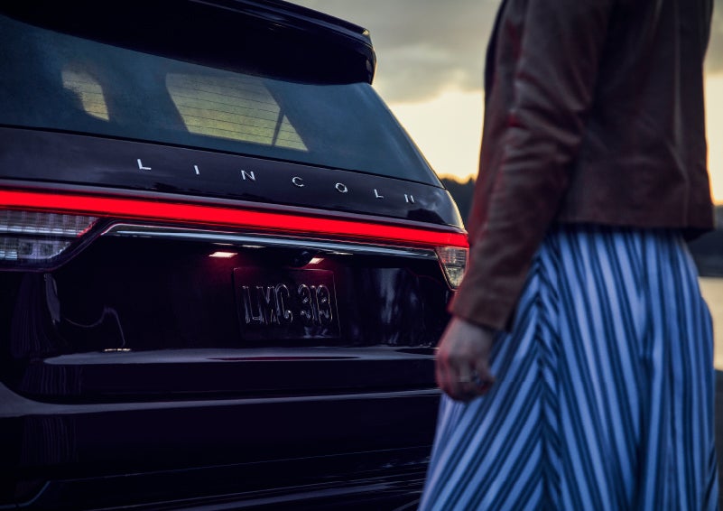 A person is shown near the rear of a 2024 Lincoln Aviator® SUV as the Lincoln Embrace illuminates the rear lights | Casa Lincoln in El Paso TX