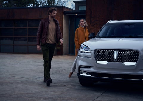 A man and a woman approaching a 2024 Lincoln Aviator® SUV, which illuminates certain lights when they are close | Casa Lincoln in El Paso TX