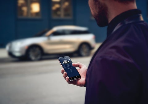 A person is shown interacting with a smartphone to connect to a Lincoln vehicle across the street. | Casa Lincoln in El Paso TX