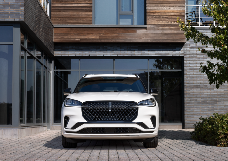 A white 2025 Lincoln Aviator® SUV is shown parked outside a modern building with gray brick and wood accents. | Casa Lincoln in El Paso TX