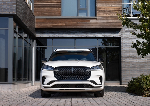 A white 2025 Lincoln Aviator® SUV is shown parked outside a modern building with gray brick and wood accents. | Casa Lincoln in El Paso TX