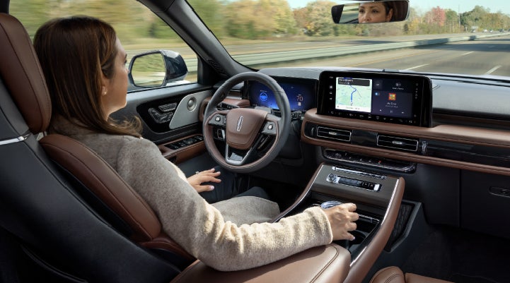 A 2027 Lincoln Aviator® SUV is being driven hands-free on a highway lined with trees. | Casa Lincoln in El Paso TX