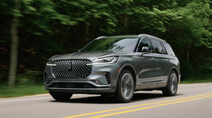 A 2027 Lincoln Aviator® SUV is being driven down a road lined with trees. | Casa Lincoln in El Paso TX